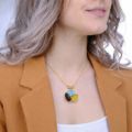 Model wearing a gold plated 925 sterling silver Baltic amber pendant necklace with lemon yellow, black, and turquoise stones, styled with a neutral blazer and white top.