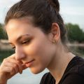 Woman wearing small rectangular Baltic green amber stud earrings set in 18K gold plated sterling silver, shown on ear in natural outdoor light