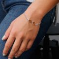 Close-up of a hand resting on blue jeans, wearing a thin silver bracelet with an infinity-shaped center and two honey-colored amber stones.