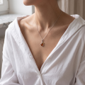 Woman wearing the Pola Baltic Amber Pendant in Sterling Silver on a delicate silver chain, styled with a white shirt in a luxury jewelry lifestyle portrait.