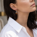 Woman wearing the Deirdre Baltic Honey Amber Earrings in Sterling Silver, showcasing genuine honey Baltic amber and polished 925 sterling silver in an elegant luxury jewelry lifestyle setting.