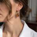 Woman wearing the Lisa Baltic Honey Amber Drop Earrings in Sterling Silver, showcasing genuine honey Baltic amber and polished 925 sterling silver in an elegant luxury jewelry lifestyle setting.