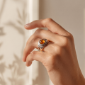 Hand wearing a sterling silver Baltic honey amber ring with a round amber gemstone in warm natural light.