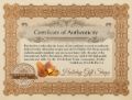 Certificate of Authenticity with an ornate brown decorative border on a cream background. The certificate states that the bearer has received authentic amber jewelry from Holiday Gift Shops, claiming compliance with International Amber Association standards and U.S. Federal Trade Commission jewelry guidelines. At the bottom are images of three amber stones, a circular 'Authentic Verified' seal with 'Holiday Gift Shops' across it, and a cursive 'Holiday Gift Shops' signature.