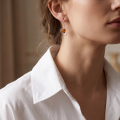 Woman wearing the Valentine Baltic Honey Amber Earrings in Sterling Silver, showcasing genuine honey Baltic amber and polished 925 sterling silver in an elegant luxury jewelry lifestyle setting.