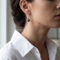 Woman wearing the Linda Baltic Green Amber Earrings in Sterling Silver, showcasing genuine green Baltic amber and polished 925 sterling silver in an elegant luxury jewelry lifestyle setting.