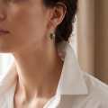 Woman wearing the Penelope Baltic Green Amber Earrings in Sterling Silver, showcasing genuine green Baltic amber and polished 925 sterling silver in an elegant luxury jewelry lifestyle setting.