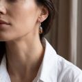 Woman wearing the Thea Baltic Honey Amber Earrings in Sterling Silver, showcasing genuine honey Baltic amber and polished 925 sterling silver in an elegant luxury jewelry lifestyle setting.