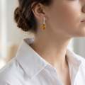 Woman wearing the Eleanor Baltic Honey Amber Drop Earrings in Sterling Silver, showcasing genuine honey Baltic amber and polished 925 sterling silver in an elegant luxury jewelry lifestyle setting.