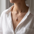 Woman wearing the Aretha Baltic Amber Pendant in Sterling Silver, showcasing genuine Baltic amber and polished 925 sterling silver in an elegant luxury jewelry lifestyle setting.
