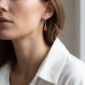 Woman wearing the Ambie Baltic Honey Amber Stud Earrings in Sterling Silver, showcasing genuine honey Baltic amber gemstones and polished 925 sterling silver in an elegant luxury jewelry lifestyle setting.