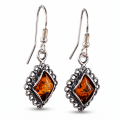 Pair of “Meryl” Baltic Honey Amber Earrings in Sterling Silver on a white background, featuring oval amber stones and ornate silver settings.